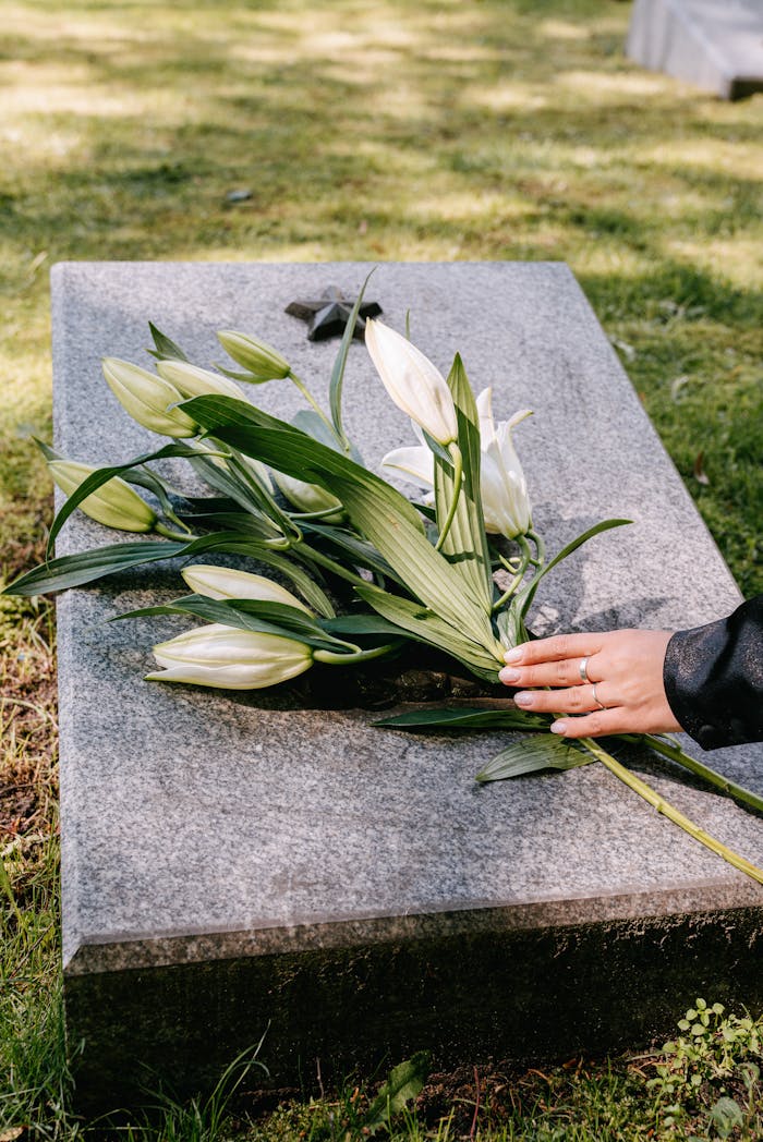 about-us White lilies on a gravestone symbolize remembrance in an outdoor cemetery setting.